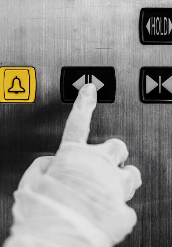 Gloved hand pressing an elevator button to prevent coronavirus contamination