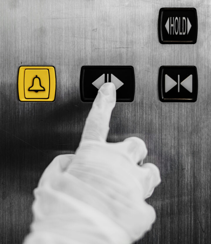 Gloved hand pressing an elevator button to prevent coronavirus contamination